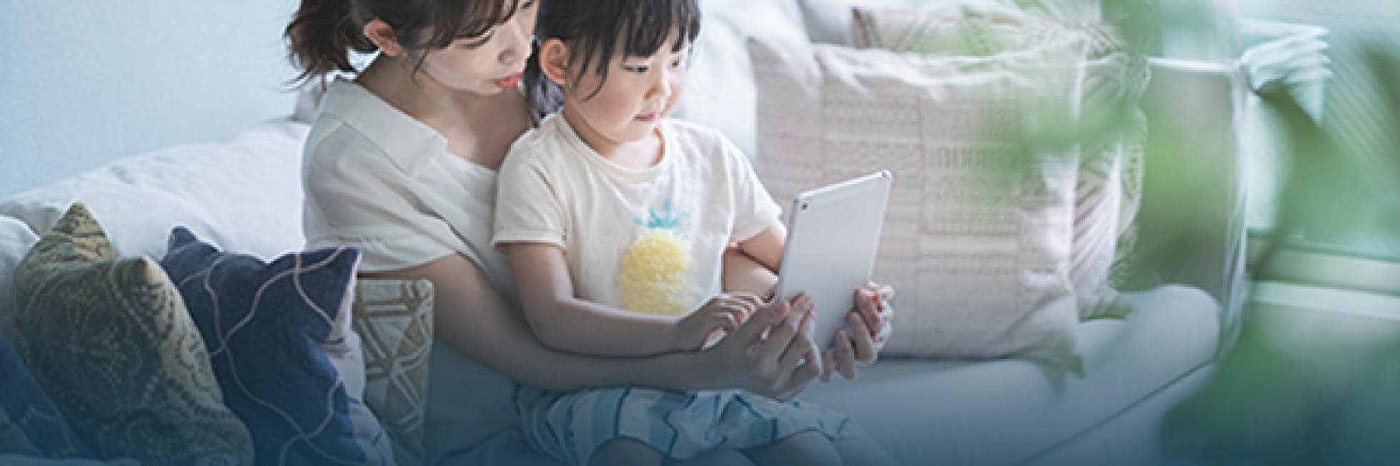 明るい部屋の中で、女性と子供がソファに座って一緒にタブレットを見ています。